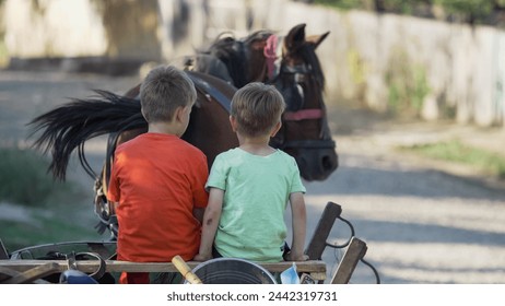 Two little brothers sit in the cart pulled by horse at countryside - Powered by Shutterstock