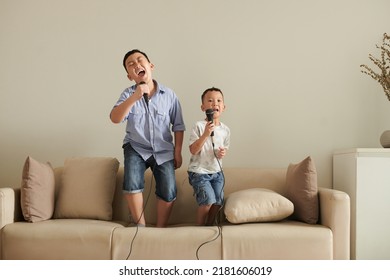 Two little brothers standing on sofa at home and singing into microphones together - Shutterstock ID 2181606019