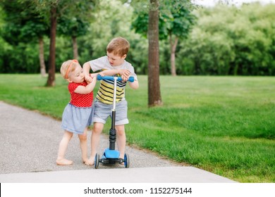 Two Little Caucasian Preschool Children Fighting Hitting Each Other. Boy And Girl Can Not Share One Scooter. Older Sibling Brother Not Giving His Toy To Younger Sister. Communication Problems.