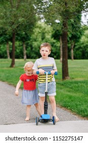 Two Little Caucasian Preschool Children Fighting In Park Outside. Boy And Girl Can Not Share One Scooter. Older Sibling Brother Not Giving His Toy To Younger Sister. Communication Problems.