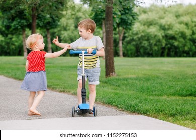 Two Little Caucasian Preschool Children Fighting In Park Outside. Boy And Girl Can Not Share One Scooter. Older Sibling Brother Not Giving His Toy To Younger Sister. Communication Problems.