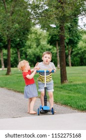 Two Little Caucasian Preschool Children Fighting In Park Outside. Boy And Girl Can Not Share One Scooter. Older Sibling Brother Not Giving His Toy To Younger Sister. Communication Problems.