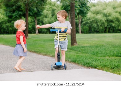 Two Little Caucasian Preschool Children Fighting In Park Outside. Boy And Girl Can Not Share One Scooter. Older Sibling Brother Not Giving His Toy To Younger Sister. Communication Problems.