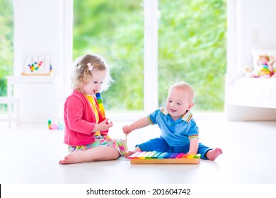 Two Little Children - Cute Curly Toddler Girl And A Funny Baby Boy, Brother And Sister Playing Music, Having Fun With Colorful Xylophone At A Window; Kids Early Development Class