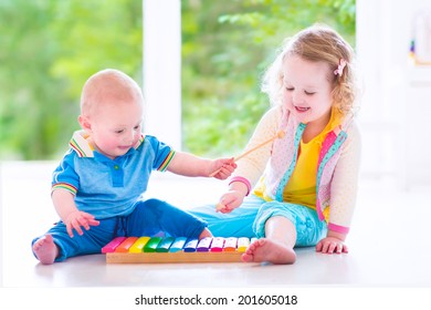 Two little children - cute curly toddler girl and a funny baby boy, brother and sister playing music, having fun with colorful xylophone at a window; kids early development class - Powered by Shutterstock