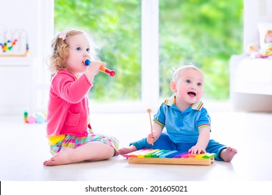 Two little children - cute curly toddler girl and a funny baby boy, brother and sister playing music, having fun with colorful xylophone and flute at a window; kids early development class - Powered by Shutterstock
