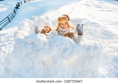 Two Little Children Have Fun Playing In A Snow Fort On A Sunny Winter Day. Winter Retro Clothes For Cold Weather.