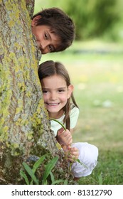 Two little children hiding behind tree