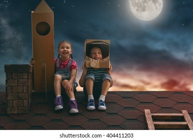 Two little children playing astronauts. Child boy in an astronaut costume and child girl with toy rocket standing on the roof of the house and looking at the sky and dreaming of becoming a spacemen.