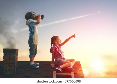 Two Little Children Playing On The Roof Of The House And Looking At The Sky And Dreaming Of Becoming A Pilots.