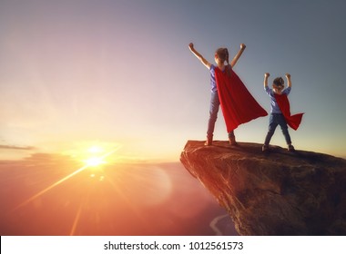 Two little children are playing superhero. Kids on the background of sunset sky. Girl power concept
