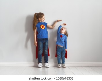 Two little children are playing superhero. Kids are measuring the growth on the background of wall. Girl power concept. 