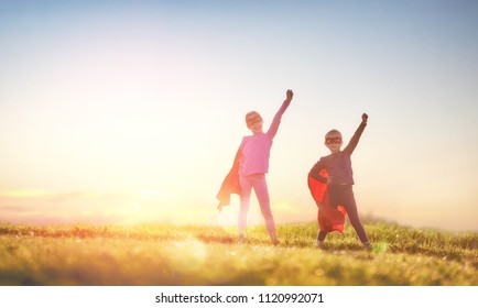 Two Little Children Are Playing Superhero. Kids On The Background Of Sunset Sky. Girl Power Concept