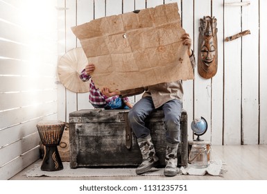 two little children study a map sitting on big old chest