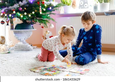 Two little chilren, cute toddler girl and school kid boy playing together card game by decorated Christmas tree. Happy healthy siblings, brother and sister having fun together. Family celebrating xmas