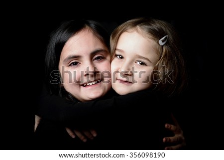Two little cute girls dressed in black posing on a black background