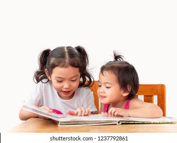 Two Little Cute Girls Sitting On Chair And Reading The Book On White Backdrop. Older Sister Read The Book  To Younger Sister. Learning And Education Of Kid.