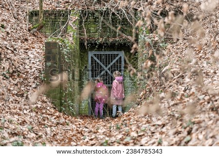 Two little girl friends kids stay at entrance of old abandoned entrance door of scary underground bunker shelter. Lost run away children in forest woods foliage danger secret building entry
