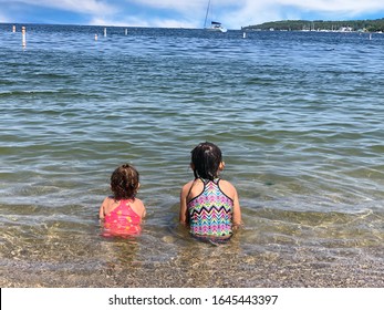 Two Little Girl Sitting Beachside Watching Sailboats Come In