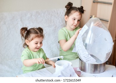 Two Little Girls With Dark Hair And Light Skin In Light Green Make A Paper Mache Craft