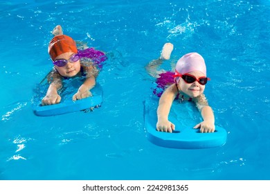 Two little girls having fun in pool learning how to swim using flutter boards