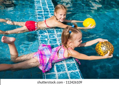two little girls holding balls in their hands and playing in the pool