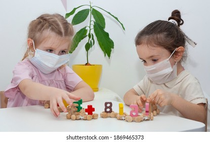 Two little girls in medical masks play constructs in the kindergarten. Little sisters play with a little train