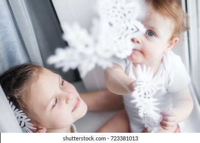 Two Little Girls Near The Window Play Snowflakes From Paper