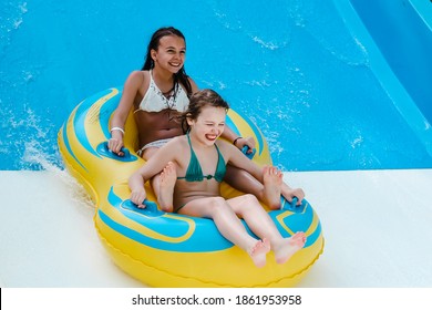 Two little girls on tube on water slide at aquapark. Summertime, vacation, entertainment, childhood concept. Colorful background.