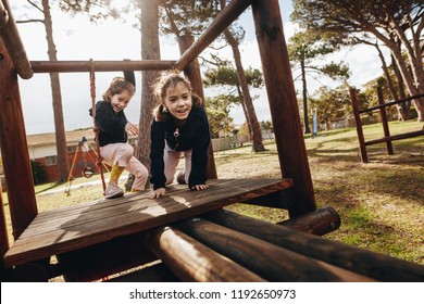 Two little girls playing at playground outdoors. Twin sisters enjoying playing on wooden structure at park. - Powered by Shutterstock