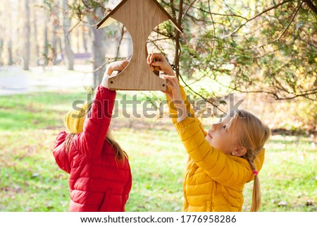 Two little girls putting food for birds at birdhouse  in the forest on warm autumn day. Children taking care of animals outdoor. Outdoor recreation and awesome adventures with kids in fall
