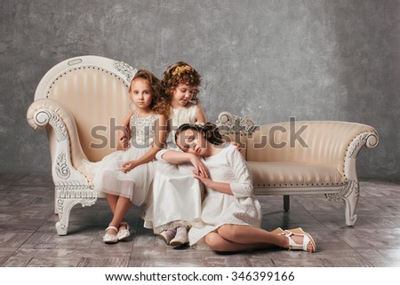Two little girls sitting on a couch in a classic style, one sitting next to a girl on the floor