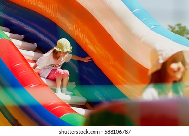 Two little girls in sun panama hats playing in inflatable bouncing castle outdoor in bright day.Happy children play outside in sun.Cute child have fun.Kids enjoy bounce house playground