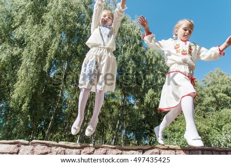two little girls in traditional Ukrainian dress jumping in the park