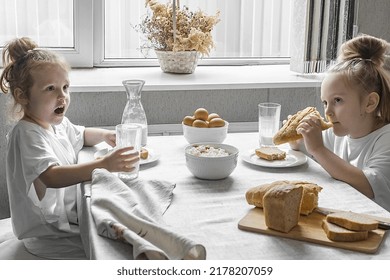 two little girls in white t-shirts have breakfast at home in the kitchen with natural and healthy products, cottage cheese and cornbread, milk and boiled chicken eggs - Shutterstock ID 2178207059