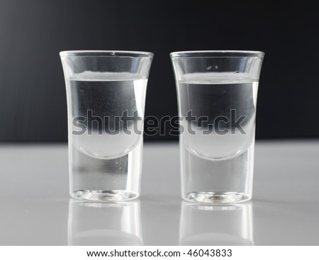 Two little glasses of transparent liquid, black in the background