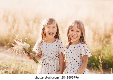 Two Little Happy Identical Twin Girls Playing Together In Nature In Summer. Girls Friendship And Youth Concept. Active Children's Lifestyle.