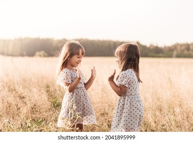 Two Little Happy Identical Twin Girls Playing Together In Nature In Summer. Girls Friendship And Youth Concept. Active Children's Lifestyle.