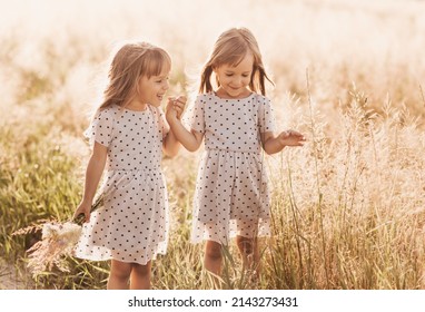 Two Little Happy Identical Twin Girls Playing Together In Nature In Summer. Girls Friendship And Youth Concept. Active Children's Lifestyle.