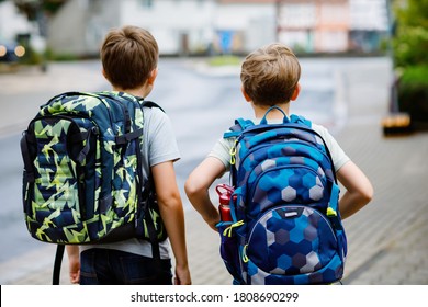 Two little kid boys with backpack or satchel. Schoolkids on the way to school. Healthy adorable children, brothers and best friends outdoors on the street leaving home. Back to school. Happy siblings.