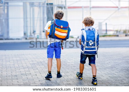 Two little kid boys with backpack or satchel. Schoolkids on the way to school. Healthy adorable children, brothers and best friends outdoors on the street leaving home. Back to school. Happy siblings.
