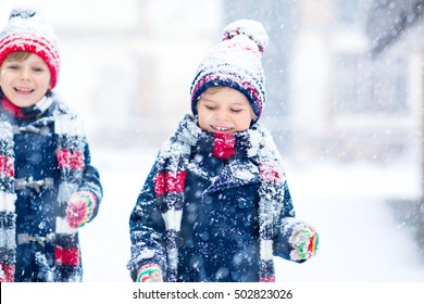 Two Little Kid Boys In Colorful Clothes Playing Outdoors During Snowfall. Active  Leisure With Children In Winter On Cold Days. Happy Siblings And Twins Having Fun With Snow