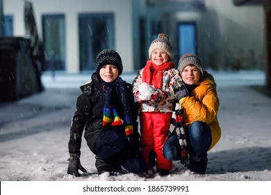 Two Little Kid Boys And Cute Toddler Girl Sitting Together Playing With Snow On Winter Night. Siblings, Brothers And Baby Sister Enjoying Strong Snowfall. Active Fun For Family Vacation