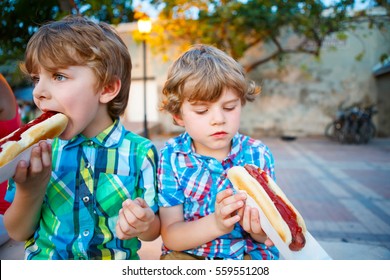 Two Little Kid Boys Eating Hot Dogs Outdoors. Siblings Enjoying Their Meal. Hotdog As Unhealthy Food For Children.