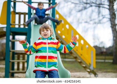 Two Little Kid Boys Having Fun And Sliding On Outdoor Playground. Funny Children, Friends And Siblings Smiling And Climbing On Slide. Summer, Spring And Autumn Leisure For Active Kids.