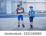 Two little kid boys with satchels. Schoolkids on the way to school. Healthy children, brothers and best friends outdoors on the street leaving home. Back to school. Happy siblings.