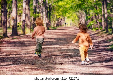 Two Little Kids Blond Boy And A Girl Run On The Alley In The Park At Summer View From Behind, Playing Catch Up