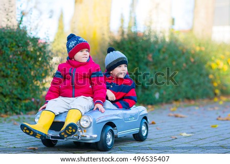 Two little kids boys in colorful clothes and rain boots driving old car and making competition, outdoors. Active leisure for children on autumn day