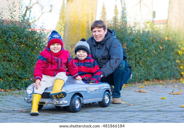 Two little kids boys in colorful\
clothes and happy dad driving old car. Father and sons making\
competition, outdoors. Active leisure for children on winter\
day
