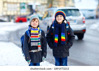 Zwei kleine Kinder Jungen der Grundschule gehen während des Schneefalls zur Schule. Fröhliche Kinder, die Spaß haben und mit dem ersten Schnee spielen. Geschwister und Freunde mit Rucksack in bunten Winterkleidung